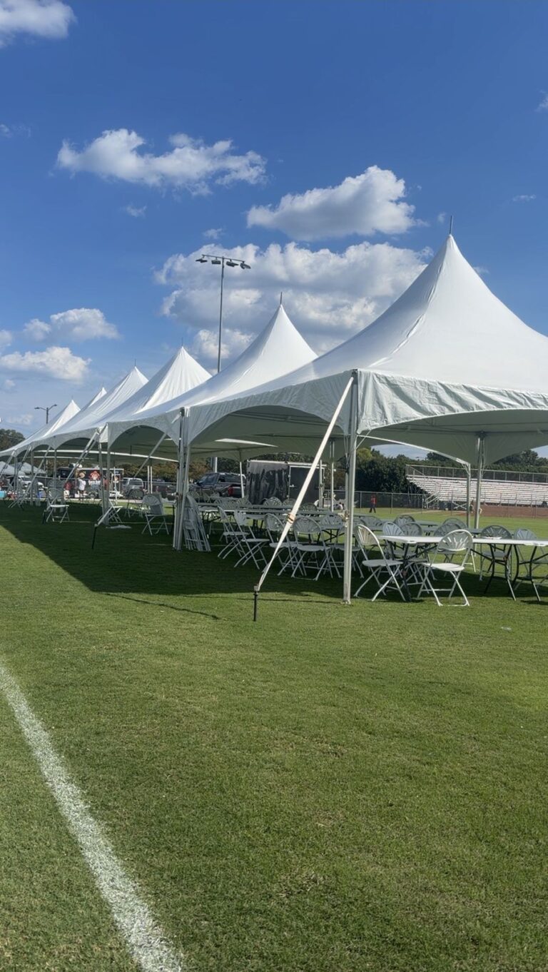 A long row of white high-peak tents with tables and chairs on a field