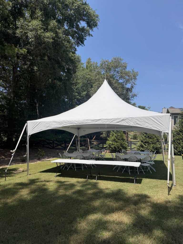 White high-peak tent with rectangular tables on a shaded lawn