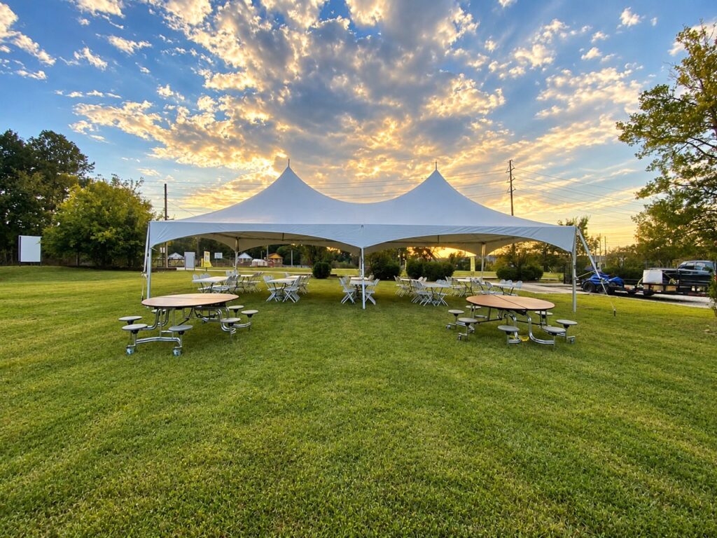 White high-peak event tent with tables and chairs on a lawn at sunset
